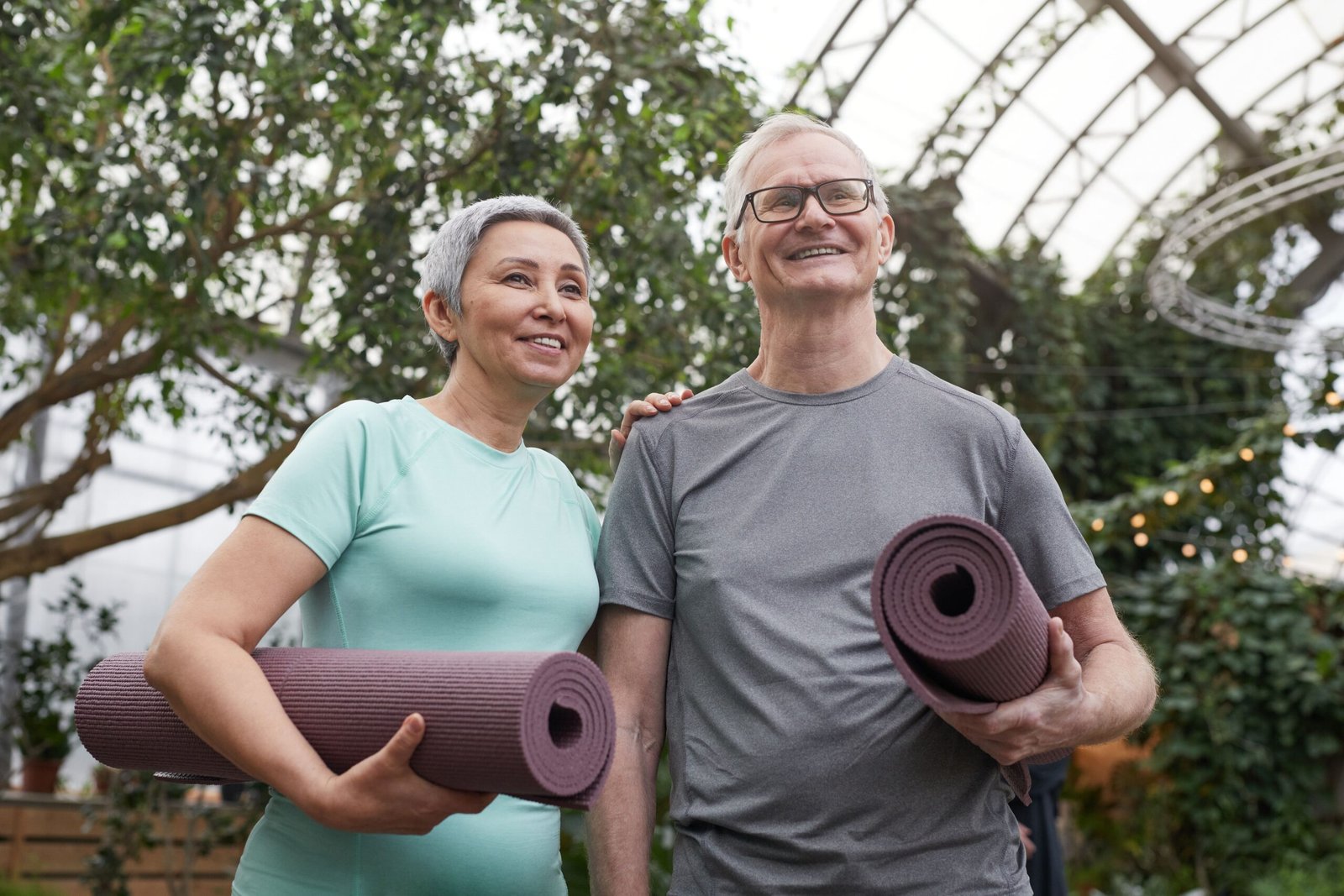 Two older adults outdoors holding exercise mats